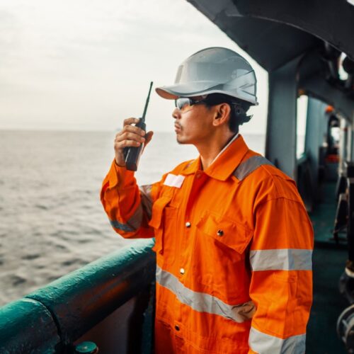 Seafarer in a hard hat using a handheld radio on a ship's deck