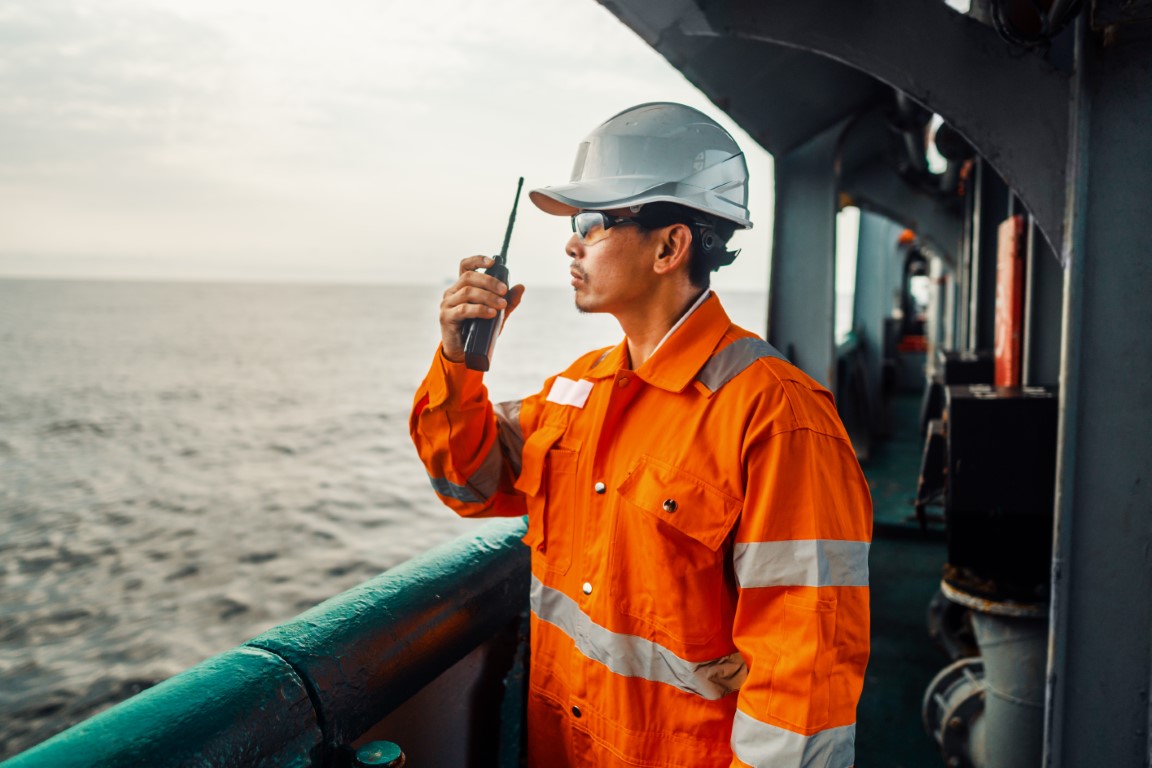 Seafarer in a hard hat using a handheld radio on a ship's deck